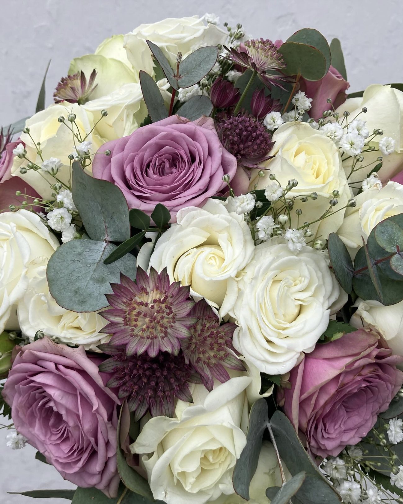 Tæt nærbillede af brudebuket med hvide og støvlilla roser, astrantia og eukalyptus – en klassiker fra Fru P